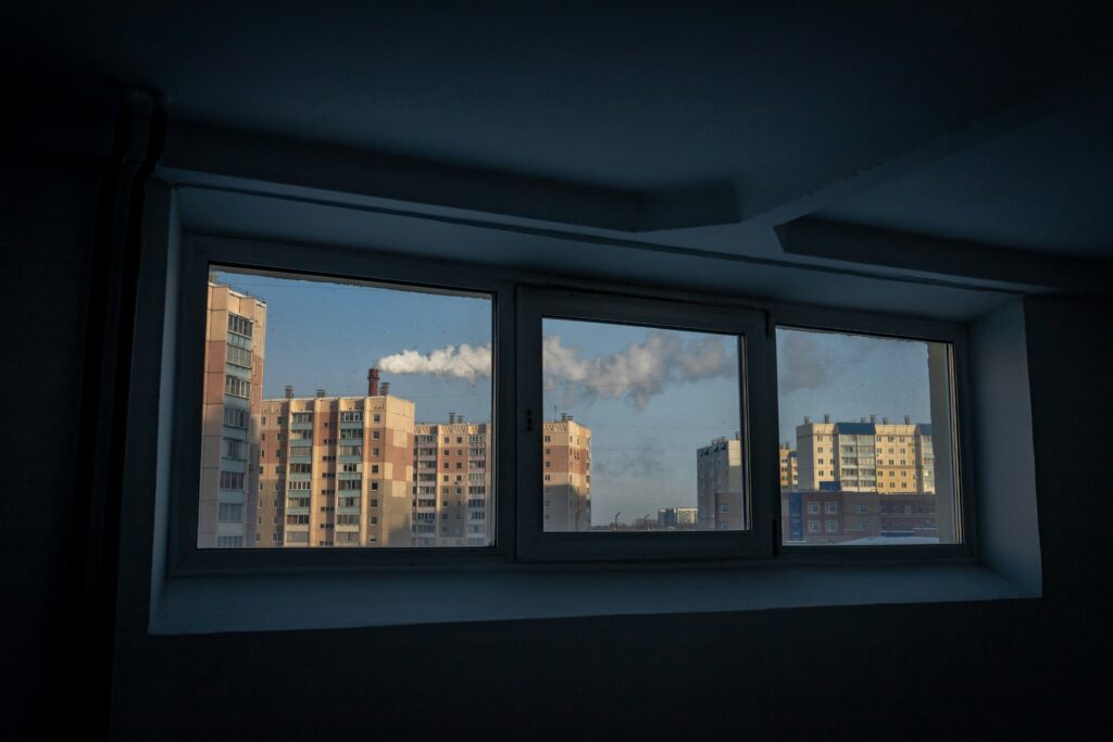 a view of buildings through a window, smoke emitting from a chimney in the distance